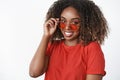 How you doing sunny. Portrait of cute african-american modern woman in red t-shirt and trendy sunglasses touching rim