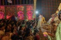 Hindu purohit spraying Holy water, called shantir jol, upon devotees worshipping Goddess Durga, inside decorated Durga Puja Pandal