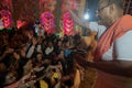 Hindu purohit spraying Holy water, called shantir jol, upon devotees worshipping Goddess Durga, inside decorated Durga Puja Pandal