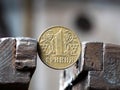 Hryvnya coin clamped in a metal vise. Currency and Ukrainian economy under the onslaught, the concept of financial problems and