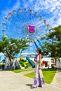 A smiling girl stand in front of the colorful ferris wheel in Santorini Park