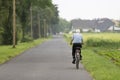 Huerth, NRW, Germany, 06 05 2021, old man driving on a bicycle on a country road between field and trees, village in the
