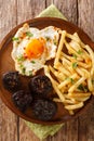 Huevos rotos con morcilla fried egg with fries and blood sausage close-up in a plate. vertical top view