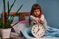 Huge alarm clock in the hands of a angry sad child girl in the bedroom. 7 o& x27;clock in the morning, stress. Royalty Free Stock Photo