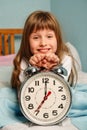 Huge alarm clock in the hands of a happy smile child girl in the bedroom. 7 o'clock in the morning. Royalty Free Stock Photo