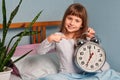 Huge alarm clock in the hands of a happy smile child girl in the bedroom. 7 o'clock in the morning. Royalty Free Stock Photo