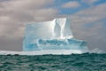 Huge antarctic table iceberg with penguins and tiny zodiac in front. Small boat with people in front of iceberg watching penguins.