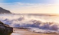 huge beautiful wave is breaking at the coastline while a breeze blows the spit water out of the sea at a wonderful sunset with