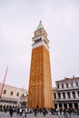 Huge bell tower made of red brick in Piazza San Marco - Campanile of St. Mark`s Cathedral in Venice, Italy. A crowd of Royalty Free Stock Photo