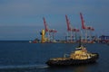 large black tugboat floating through the water by cranes and cranes