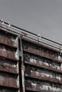 Huge bolted steel wall with pipes along the top, gray sky