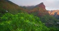 Huge cliff in a spring sunset, green bushes on mountain slope, little village in the valley. Cloudy coloured sky in the Royalty Free Stock Photo