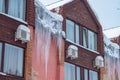 Huge dangerous icicles of ice hang from the roof of the house in winter or spring