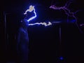 Huge electric coils spew lightning striking a man dressed in a chain suit. Electric show