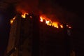 Huge fire blazing in multistory apartment building. Burning house is engulfed in flames at night during the disastrous