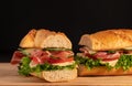 Huge fresh crispy baguette sandwich with meat, prosciutto, cheese, lettuce salad and vegetables. Close up. Black background. Space Royalty Free Stock Photo