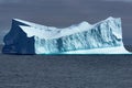 Huge Iceberg with escarpment shining turquoise on grey day in Greenland