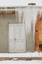 Huge icicles hang from the roof of an abandoned house with wooden door Royalty Free Stock Photo