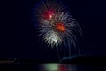 A huge multicolored firework ball over a big night city is reflected in the river