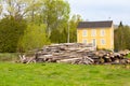 Huge pile of tree trunks in front of yellow clapboard house in rural area in the spring