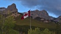 Huge red and white Canadian flag flying in the wind between trees in front of mountains near Canmore, Kananaskis Country, Canada. Royalty Free Stock Photo