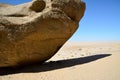 A huge rocky boulder lies in the desert under a blue sky