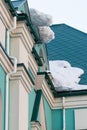 A huge snow block hangs from the roof above the entrance to the building.