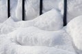 A huge snowdrift of white, crystalline, layered snow near the fence