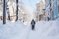 Huge snowdrifts on the city streets after a snowstorm. People have difficulty walking on the street, some use ski poles