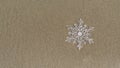 Huge sparkling snowflake on the sand in the sea foam. Concept of Winter and Christmas vacation on the beach Royalty Free Stock Photo