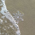 Huge sparkling snowflake on the sand in the sea foam. Concept of Winter and Christmas vacation on the beach