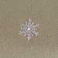 Huge sparkling snowflake on the sand in the sea foam. Concept of Winter and Christmas vacation on the beach and resort. Royalty Free Stock Photo