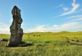 A huge stone menhir standing in the center of a vast meadow surrounded by hills on a sunny summer day