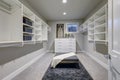 Huge walk-in closet with shelves, drawers and gray bench.