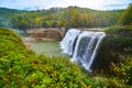 Huge waterfall wide angle up close pouring over cliffs into canyon in lush green forest with hints of approaching fall