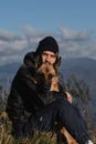 Hugging best friend in nature. Young handsome Caucasian man with beard is sitting on top of mountain next to his dog and enjoying Royalty Free Stock Photo