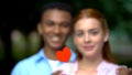 Hugging multiethnic teen couple holding paper heart, tender relationship, love