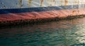 Hull of a ship with a red and blue stripe pattern, showing signs of rust and weathering. Royalty Free Stock Photo