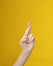 Human arm with crossed fingers on yellow background. Luck, superstition hand gesture