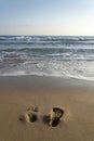 Human barefoot footprints in sand heading to sea awaiting incoming wave