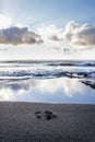 Human barefoot footprints in sand heading to sea awaiting incoming wave, sunny cloudy sunrise, active healthy living concept