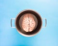 A human brain in a cooking pot on a light blue pastel background. Flat lay