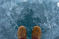 Human in brown nubuck boots is standing on cracked blue ice