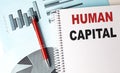 HUMAN CAPITAL text on a notebook with pen on a chart background