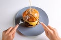 A human cuts a homemade cheeseburger with cutlery with a knife and fork on a gray plate on a white background. Hands in Royalty Free Stock Photo