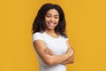 Human emotions. Happy young african american woman with curly hair posing with crossed arms over yellow background