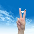 Human or female hands with two fingers painted with a red heart and smiley faces over cloud blue sky Royalty Free Stock Photo