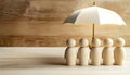 Human figures under umbrella on light wooden table. Insurance concept Royalty Free Stock Photo