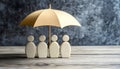 Human figures under umbrella on light wooden table. Insurance concept Royalty Free Stock Photo