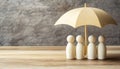 Human figures under umbrella on light wooden table. Insurance concept Royalty Free Stock Photo